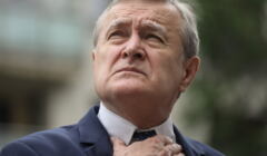 Minister Gliński patrzy do góry, jedną ręką poprawia węzeł krawata