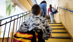 Szkoła w Bezwoli ma być zlikwidowana. Na zdjęciu chłopczyk wczhodzi po schodach, przed nim kobieta z zasłoniętą głową prowadzi córkę