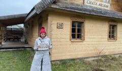 Klaudia Jachira stoi na tle drewnianego domu z kartką, na której jest napisane Biuro Poselskie