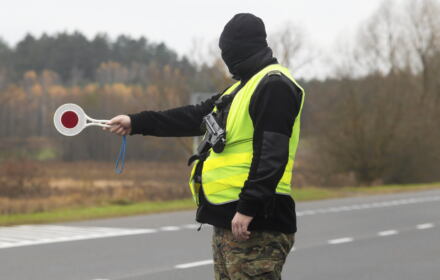 Zamaskowany męzczyzna w żołtej kamizelce zatrzymuje ruch czerwonym sygnalizatorem