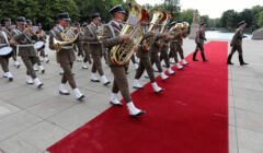 Żołnierze z orkiestry wojskowej wchodzą na czerwony dywan marszowym krokiem