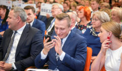 Krzysztof Brejza podczas kampanii wyborczej 2019 siedzi w pierwszym rządzie i przegląda smartfona