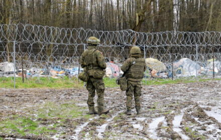 Żołnierze na granicy polsko-białoruskiej przez płotem z drutu kolczastego