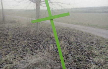 Drewniany krzyż pomalowany na zielono na polu obok drzewa