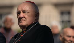 Oślepiony światłem kardynał Kazimierz Nycz mruży oczy.