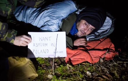 Firaz z Syrii w lesie w śpiworze z kartką - proszę o azyl w Polsce