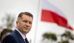 Przemysław Czarnek stoi na tle biało-czerwonej flagi