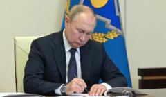 Władimir Putin siedzi za biurkiem z piórem w ręku i podpsuje dokument