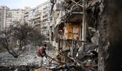 Mężczyzna próbuje porządkować okolice zbombardowanego budynku na przedmieściach Kijowa