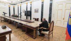 Mężczyzna (Putin) na szczie bardzo długiego stołu, na drugim końcu - dwaj mężczyźni
