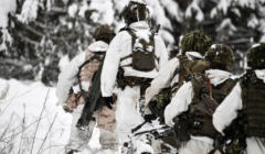 Żołnierze w maskujących strojach idą przez zimowy las
