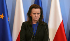 Gertruda Uścińska, stoi na tle flag polskiej i unijnej