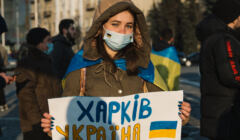 Ołesia Dekusz w zimowej kurtce i maseczce trzyma plakat 