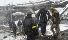 Żołnierze ukraińscy pomagają osobie o kulach przejść po zaimprowizowanym moście