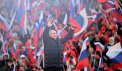 Putin wznosi ręce do góry, w tle - tlum z rosyjskimi flagami na widowni stadionu