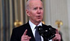 Joe Biden, mężczyzna, starszy, stoi prze mikrofonem i trzyma uniesioną rękę