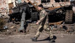 Żołnierz z emblematem Ukrainy na ramieniu, w tle - zniszczone rosyjskie czołgi