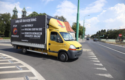Żółty furgon dostawczy - na czarnej plandece namalowane białą farbą homobiczne hasła