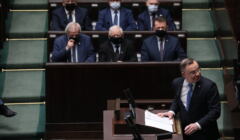 Prezydent Duda na mównicy sejmowej podczas obrad Zgromadzenia Narodowego. W tle prezes PiS Jarosław Kaczyński