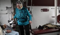 Starsza kobieta z zabandażowaną głową idzie o lasce przez medyczny pociąg ewakuujący chorych i rannych na zachód Ukrainy.