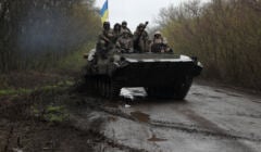 Żołnierze jadą na transporterze opancerzonym z ukraińską flagą