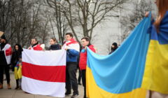 Ludzie na tlke drzew wparku stoją i trzymaja wielkie flagi Ukrainy i wolnej Białorusi