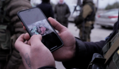 Mężczyzna w mundurze pokazuje zdjęcia ofiar na telefonie.