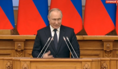 Mężczyzna (Putin) przemawia gestykulując i mrużąc oko