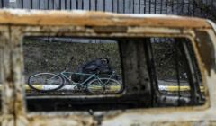 Przez okno spalonego samochody widac pobocze drogi i zabitego rowerzystę razem z jego rowerem