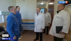Mężczyźni w piżamach na stojąco rozmawiają z Putinem w białym fartuchu