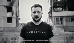 Prezydentr Zełenski z koszulce z napisem Im Ukrainian na tle zburzonego domu mieszkalnego