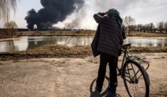 Mężczyzna stoi i patrzy na unoszący się dym po tym, jak rosyjskie rakiety uderzyły w magazyn paliwa w mieście Kałyniwka, 25 marca 2022 r.
