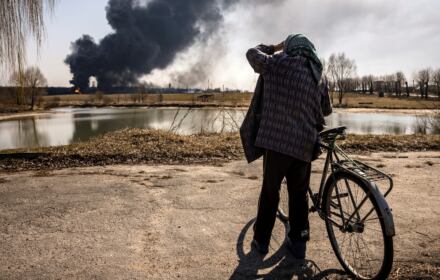 Mężczyzna stoi i patrzy na unoszący się dym po tym, jak rosyjskie rakiety uderzyły w magazyn paliwa w mieście Kałyniwka, 25 marca 2022 r.