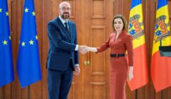 Ubrany w garnitur szef Rady Europejskiej Charles Michel wita się z ubraną ciemno czerwoną sukienkę prezydentkę Mołdawii Maię Sandu. W tle flagi UE i Mołdawii