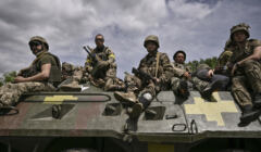 Żołnierze z żółtymi opaskami siedzą na wozie bojowym