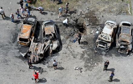 zniszczone pociskiem samochody sfotografowane z góry, wokół nich ludzie
