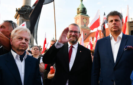Trzech mężczyzn pod kolumną Zygmunta, w tle flagi