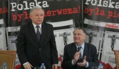 Starszy mężczyzna stoi, obok przy stole siedzi drugi, Kaczyński i Olszewski