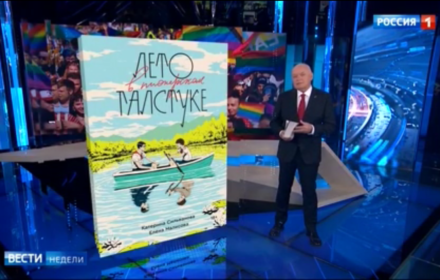 Studio telewizyjne, prowadzący a obok wielkie zdjęcie książki po rosyjsku "Lieto w pionierskom gałsztukie". Na okładce dwóch chłopców w łódce