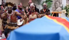 afrykańscy tancerze w ludowych strojach nad trumną przykrytą flagą