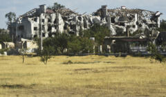 zrujnowany bombardowaniem duży budynek, na pierwszym planie łąki