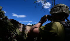 Żołnierz w okopie patrzy przez lornetkę na niebieskie nieo