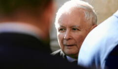 Jarosław Kaczyński rozmawia z dwoma mężczyznami odwróconymi plecami do aparatu