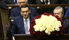 Mateusz Morawiecki w Sejmie, w ławach rządowych. Po jego lewej stronie, zasłonięty wiązanką biało-czerwonych kwiatów, wicepremier Piotr Gliński