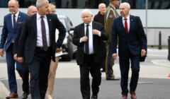 Jarosław Kaczyński idzie przez plac Piłsudskiego w otoczeniu ochrony, w tle stoi żołnierz