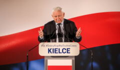 Jarosław Kaczyński przemawia na tle biało-czerwonej flagi