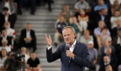 Mężczyzna z mikrofonem w ręku przemawia unosząc rękę, Donald Tusk
