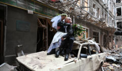nowożeńcy pozują na wraku samochodu w zbombardowanym budynku