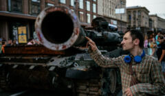Mężczyzna dotyka lufy zniszczonego rosyjskiego czołgu