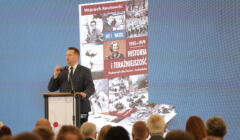Minister Przemysław Czarnek przemawia na tle wyświetlonej okładki podręcznika do przedmiotu Historia i Teraźniejszość